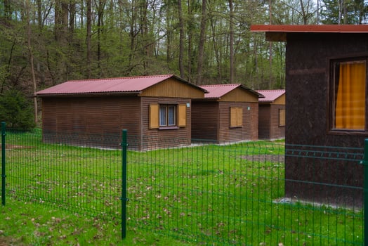 Wooden cabins with closed shutters and red roofs in fenced green area in forest, spring, atmosphere photo