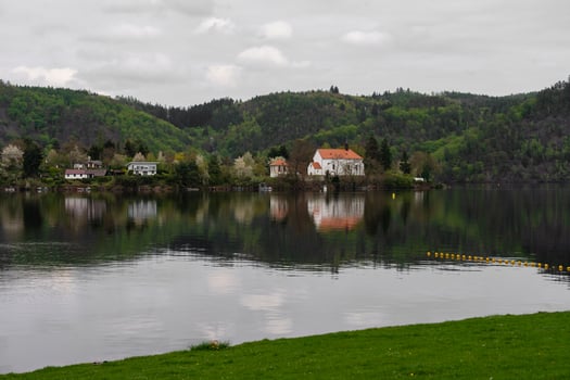 Church and houses reflected in calm river with spring forest in background - rural Czech landscape photo