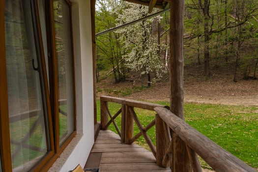 Rustic wooden porch of house with open window and spring forest view, green grass and blooming tree photo