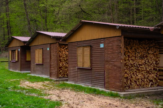 Wooden cabins with shuttered windows, stacked firewood in forest, traditional rural architecture photo