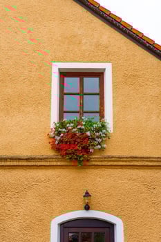 Rustic window with red and white blooming flowers on ochre stucco wall of European house facade photo