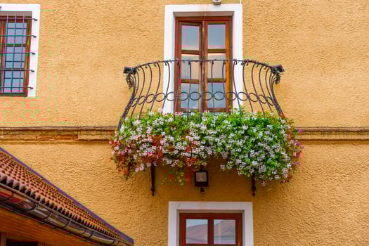 Colorful flowers on iron balcony of ochre house with wooden windows - European architectural detail photo