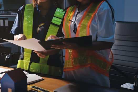 Two women in safety vests and hard hats working at a desk photo