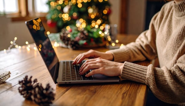 Cozy atmosphere with person typing on laptop, surrounded by festive decorations and Christmas tree in background, creating warm and inviting holiday spirit photo