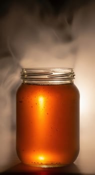 Glass jar filled with golden honey with smoke rising photo
