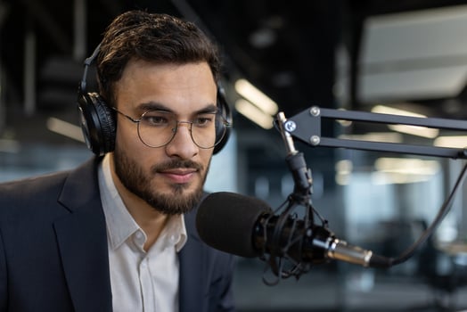 A man wearing headphones speaks into a microphone, likely for a podcast or radio show, with a focused expression. photo