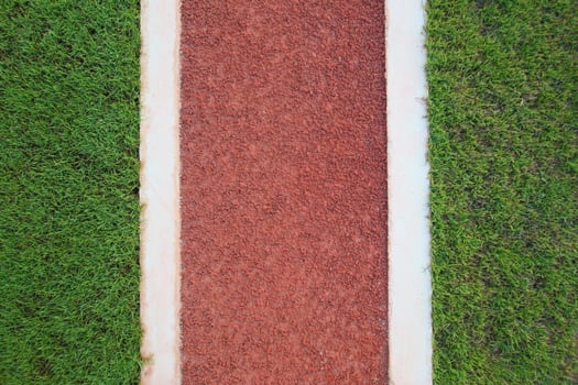 A top-down view of a red walking path dividing fresh green grass on both sides. Symmetrical layout with vibrant colors, ideal for abstract nature backgrounds or fitness themes. photo