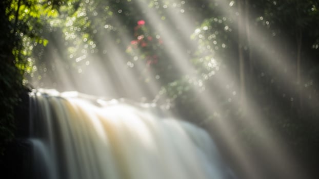 A waterfall in the jungle with sunlight streaming through the trees photo