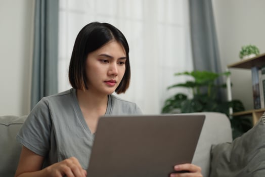 Front view, Young Asian woman in casual clothes using laptop while sitting on sofa in cozy living room. Work from home, Remote working. photo