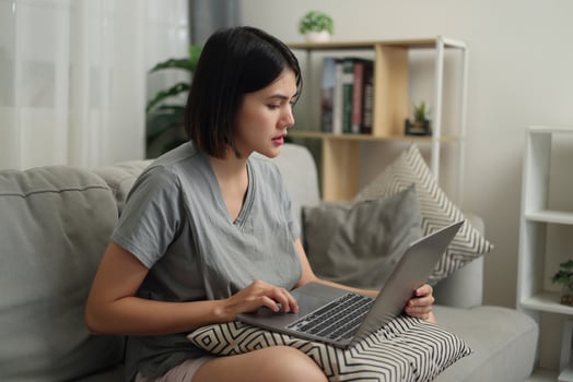 Side view, Young Asian woman in casual clothes using laptop while sitting on sofa in cozy living room. Work from home, Remote working. photo