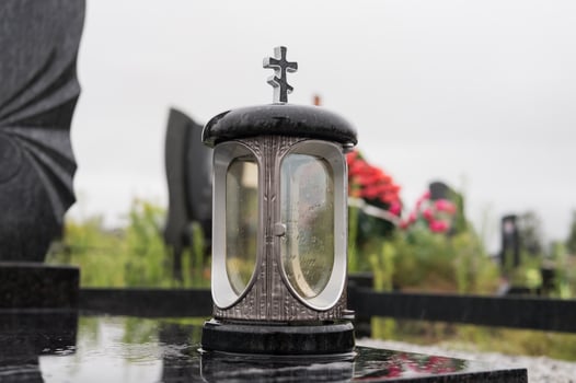 Cemetery candle lantern with cross on reflective tombstone in overcast weather photo
