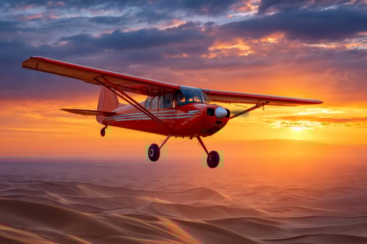 Red airplane flying over desert sand dunes at sunset photo