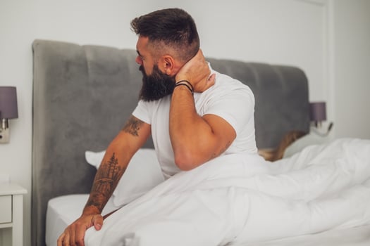 A young man wakes up in bed, stretching to ease neck pain after a restless night, illustrating everyday morning discomfort. photo