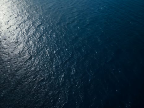 Photo of aerial view of the deep blue sea water surface with sun reflection, creating a mesmerizing texture and pattern, perfect for backgrounds and adding a touch of natures
