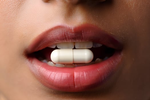 Woman holding a white capsule between her lips, about to take medication photo