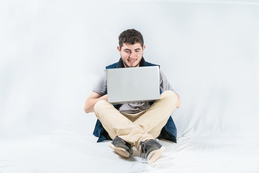 Happy guy using laptop sitting on isolated background. Cheerful freelancer sitting using laptop isolated photo