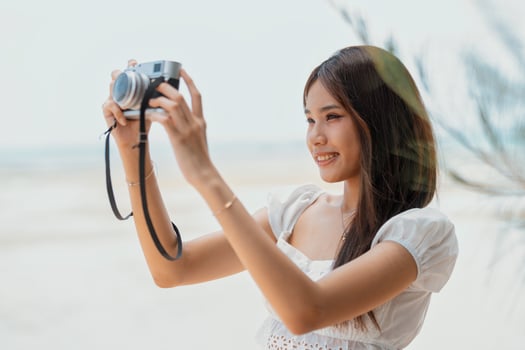 Young woman captures memories with camera at serene beach during sunny day photo