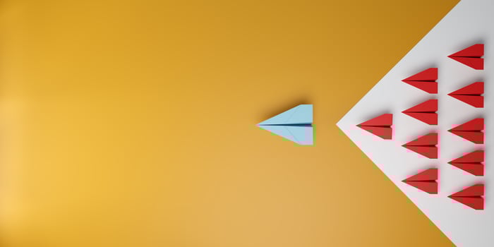 3D illustration of a blue paper plane leading a group of red planes in arrow shape on orange background. Symbol of leadership, innovation, success, and standing out. photo
