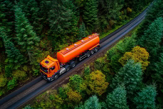 An orange tanker truck driving down a road in the forest photo
