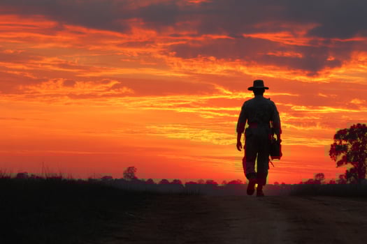A man in a hat walking down a dirt road at sunset photo