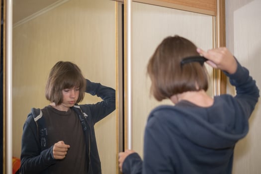 Teen brushes hair in front of mirror while reflecting on the day in a cozy room during afternoon hours photo