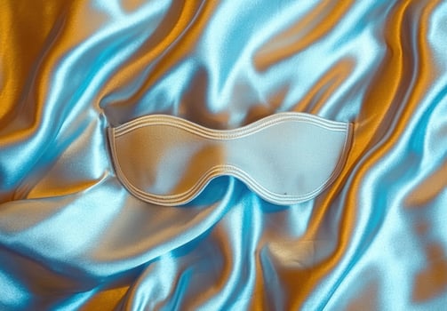 Satin sleep mask on shimmering blue and gold fabric photo