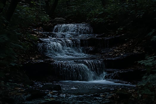 Dark Forest Waterfall Cascading Through Lush Green Foliage and Rocks. photo