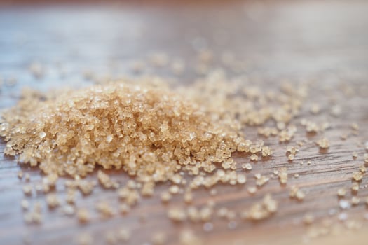 Sugar granules scattered on wooden surface close up photo