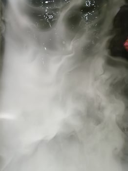 Image shows swirling white smoke or vapor with dark background, creating mysterious and ethereal atmosphere. smoke appears dense and flowing, with some reflections visible on surface photo