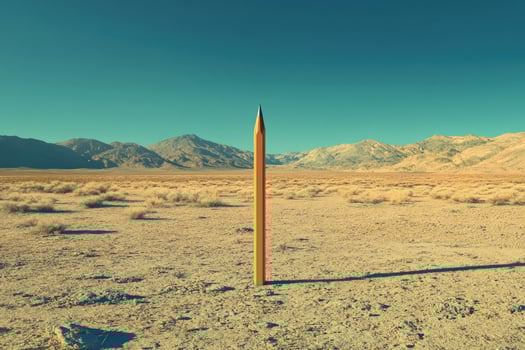 A tall pencil stands vertically within the vast desert landscape under a clear sky photo