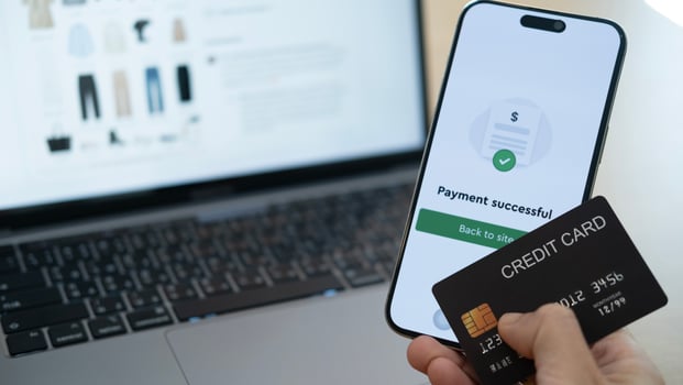 Using smartphone to confirm a payment while holding a credit card in front of a laptop, illustrating seamless device connectivity and easy digital payment photo