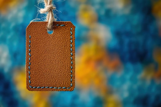 Leather tag with blue stitching hangs from twine against a blurred background photo