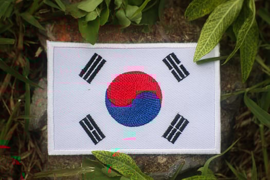 Hand-stitched Korean flag on a forest stone with grass and leaves. Natural sunlight and soft tones create a peaceful image for eco-tourism and climate-related themes. photo