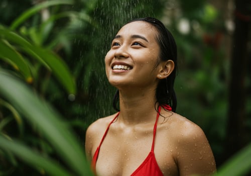 Happy woman in red swimsuit takes a refreshing shower in the lush forest photo