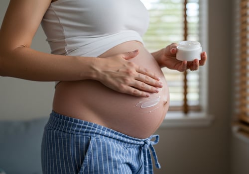 Pregnant woman applies cream to belly in bedroom for healthy skin elasticity photo