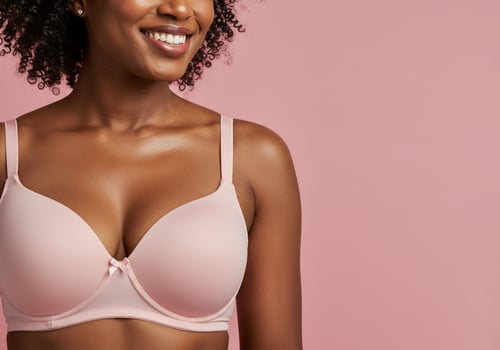 Woman in pink bra poses smiling against a pink background for intimates ad photo