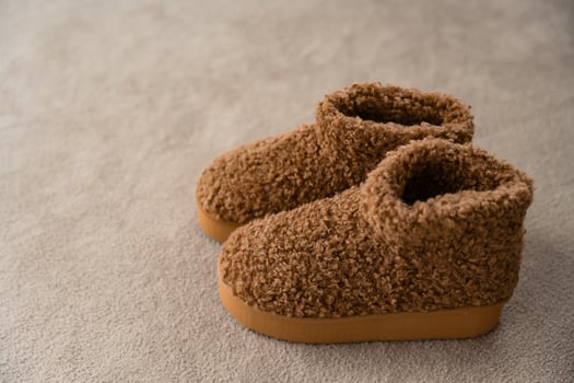 Warm brown fleece boots with textured sole and curly wool upper on soft beige carpet, copy space photo