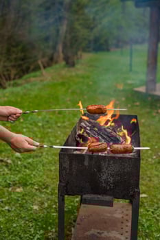 Grilling sausages on skewers over open flame in metal barbecue grill during outdoor cookout . photo