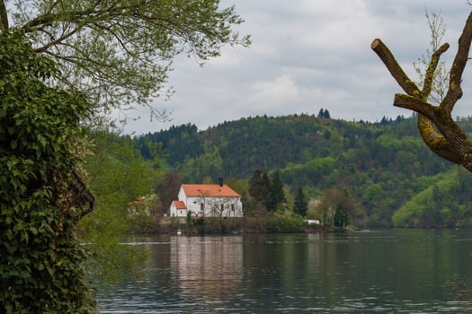 White church with red roof by forested riverbank - peaceful spring landscape with cloudy sky photo