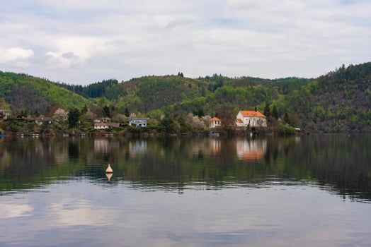 Riverside village with forested hills and cottages reflected in calm water near Nova Zivohost photo
