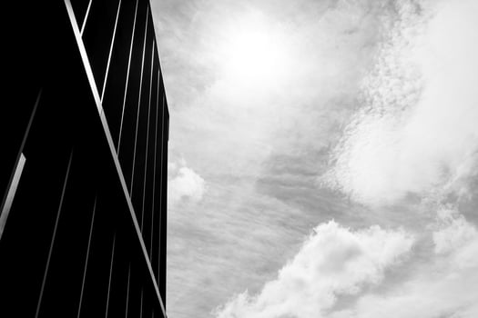Black and white photo of a modern building with vertical lines silhouetted against a bright cloudy sky. Suitable for illustrating architecture, minimalism, or urban design concepts.