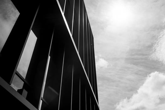 Black and white photo of a modern building facade with vertical lines, captured from a low angle against a bright sky. Suitable for illustrating architecture, urban design, or contemporary construction themes.