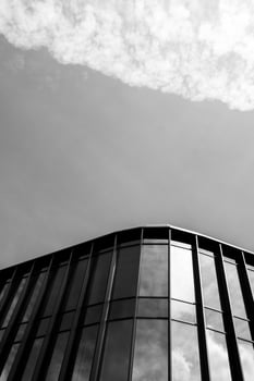 Contemporary glass building facade with reflective windows and vertical lines, set against a cloudy sky in black and white. Suitable for illustrating modern architecture, urban design, or business concepts. photo