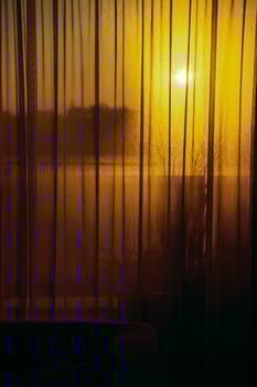 Golden sunset light shining through sheer curtains and foggy window indoors photo