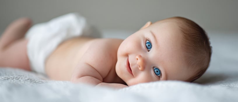 The adorable baby with bright blue eyes smiling happily on the soft surface. photo