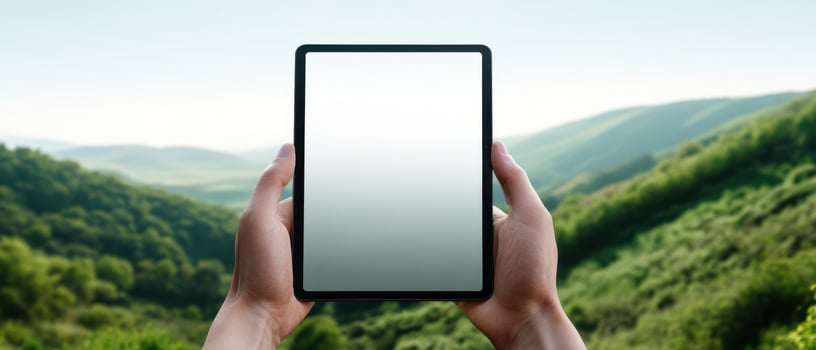 The tablet held in hands against a serene mountain landscape backdrop. photo