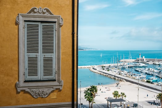Charming Mediterranean Seaside View with Vibrant Shuttered Window and Scenic Marina Vista photo