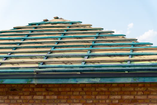 Construction workers are installing shingles on a new roof of a house, with clear skies visible in the background photo