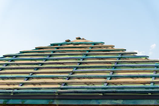 Wooden framework of a roof under construction, featuring blue-green planks against a clear sky, indicating ongoing building activity photo