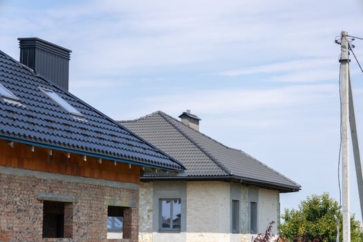 Two houses in various stages of completion are situated in a peaceful suburban area, featuring a blue sky overhead and power lines nearby photo